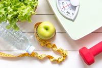 Weight loss image with a scale, healthy food, water and weights.