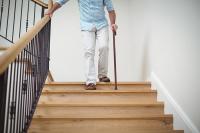 Man holding railing and walking down stairs with cane to prevent falling.