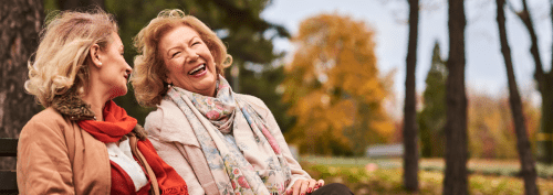 Two older women laughing on a park bench