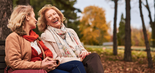 Two older women laughing on a park bench